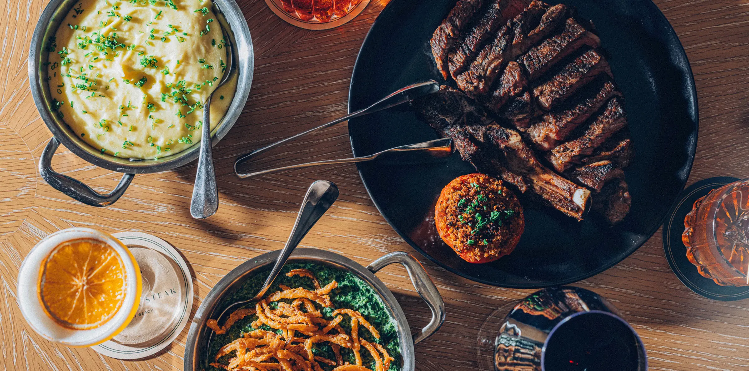 Overhead spread of steak, sides, and cocktails at Bourbon Steak by Chef Michael Mina at The Seagate Hotel