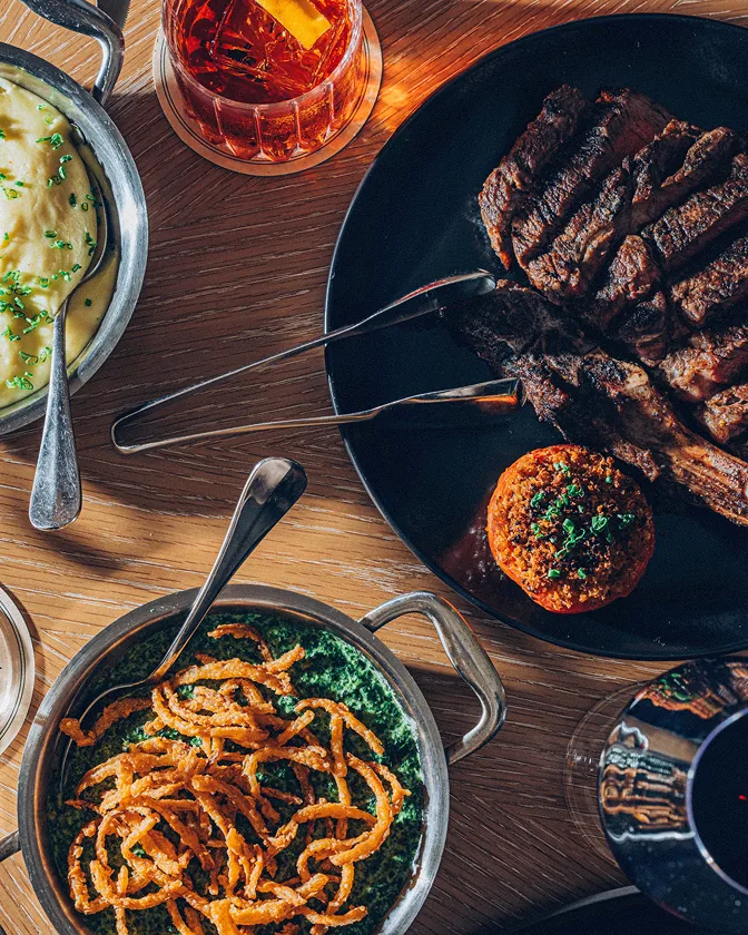 Overhead spread of steak, sides, and cocktails at Bourbon Steak by Chef Michael Mina at The Seagate Hotel