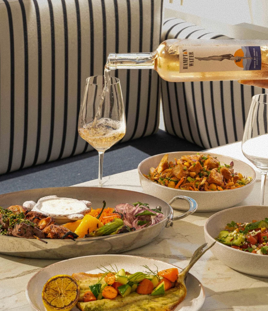 Table set with fresh seafood dishes and wine being poured at Mr. Seas restaurant inside The Seagate Beach Club