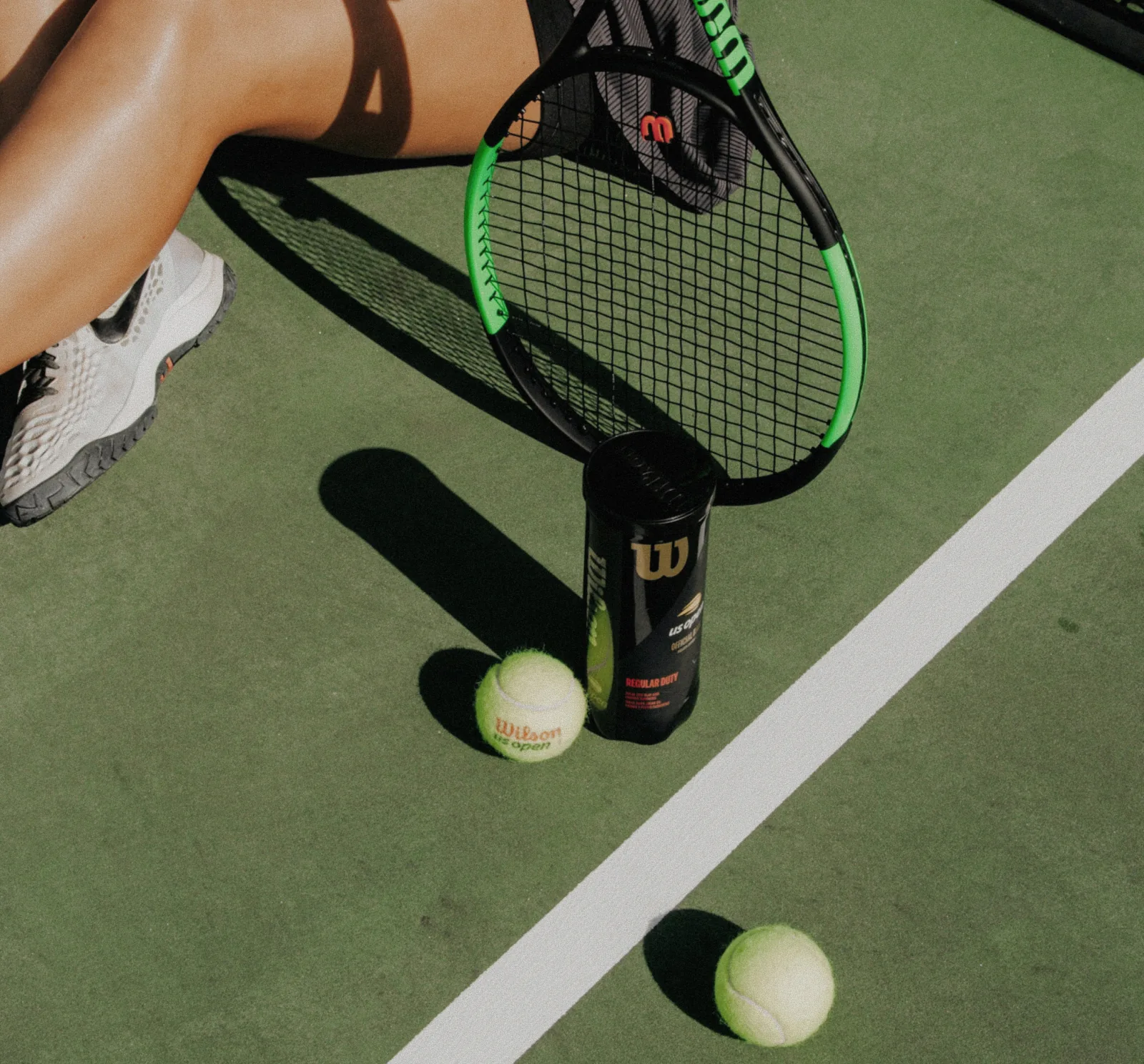 Woman seated on a tennis court holding a racquet with tennis balls at The Seagate Delray Racquet Club