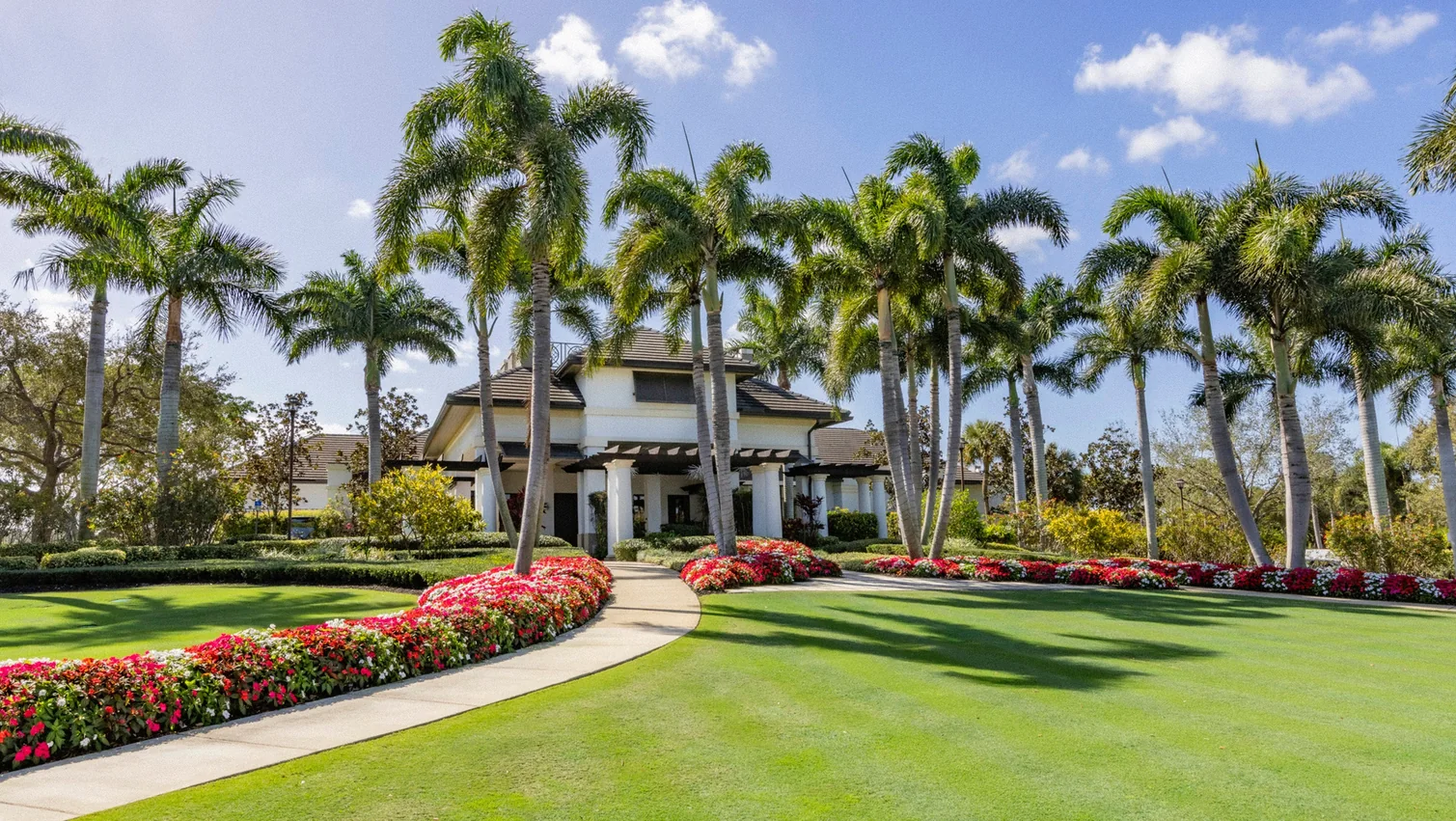 Grand entrance to The Seagate Golf Club with manicured lawn, flowering landscaping, and tall palm trees