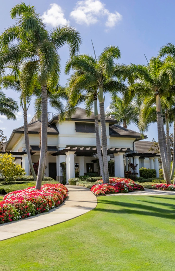 Grand entrance to The Seagate Golf Club with manicured lawn, flowering landscaping, and tall palm trees