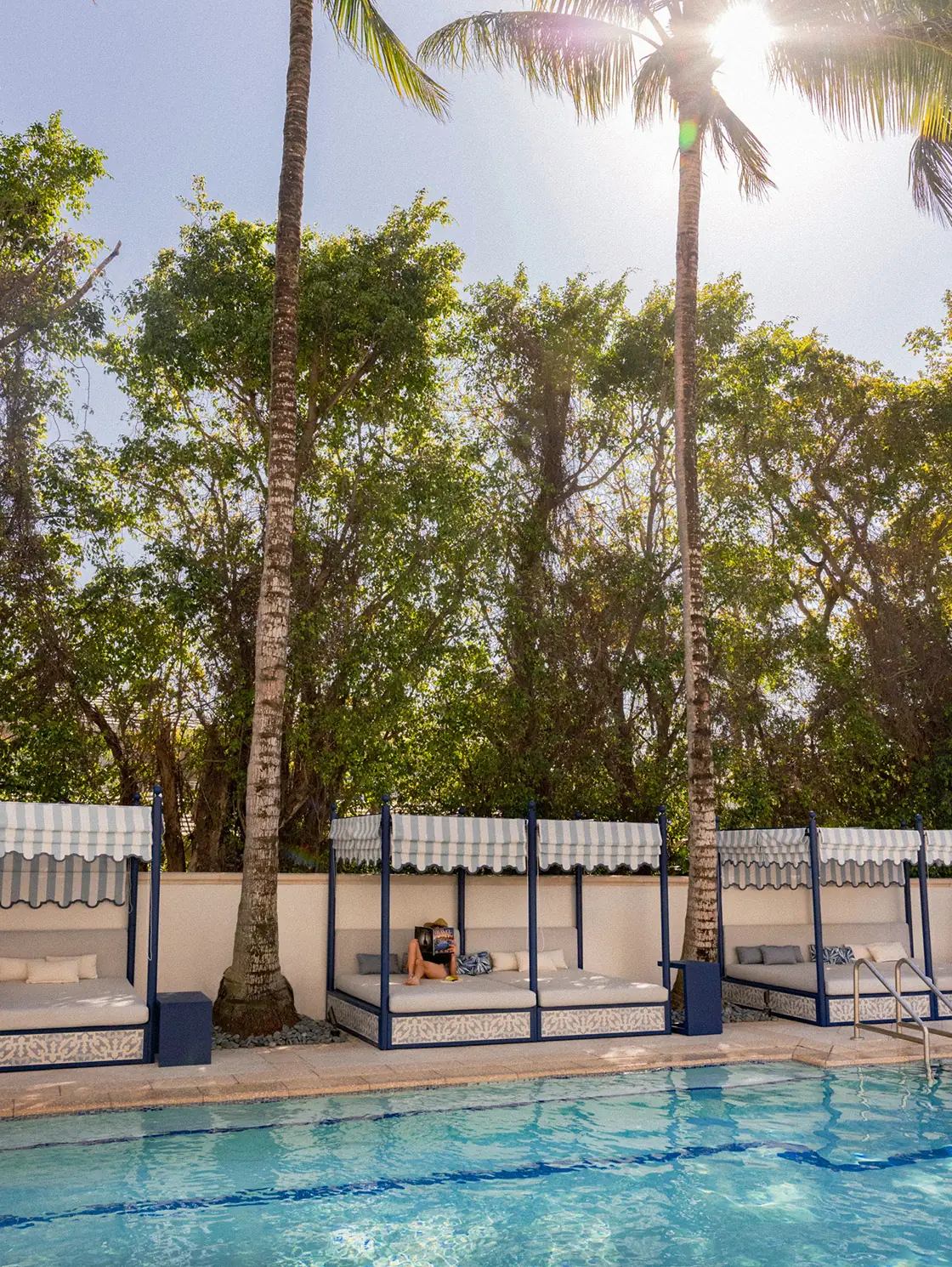 Tall palm trees in bright sun framing the pool and private cabanas at The Seagate Hotel
