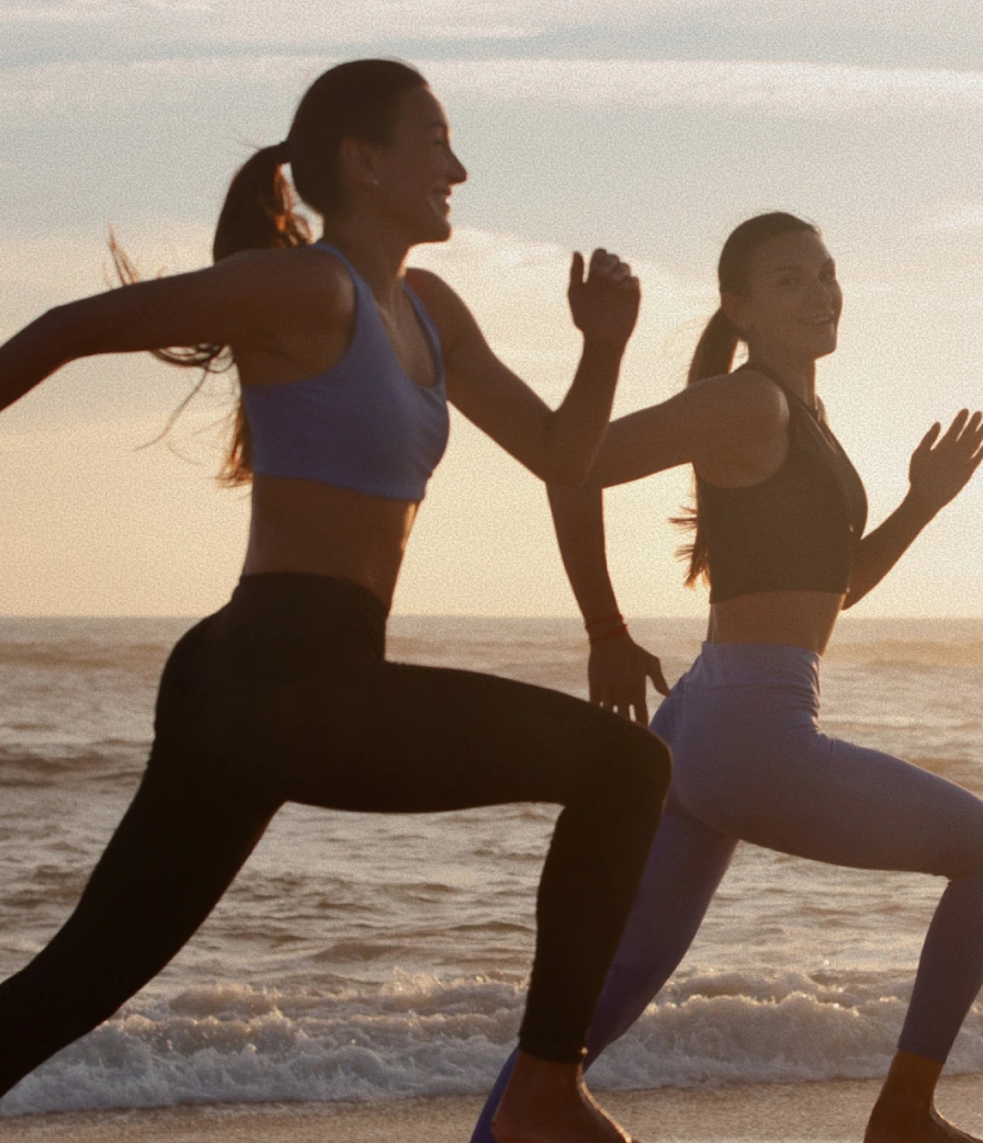 Two women running barefoot along the beach shoreline at sunset near The Seagate in Delray Beach