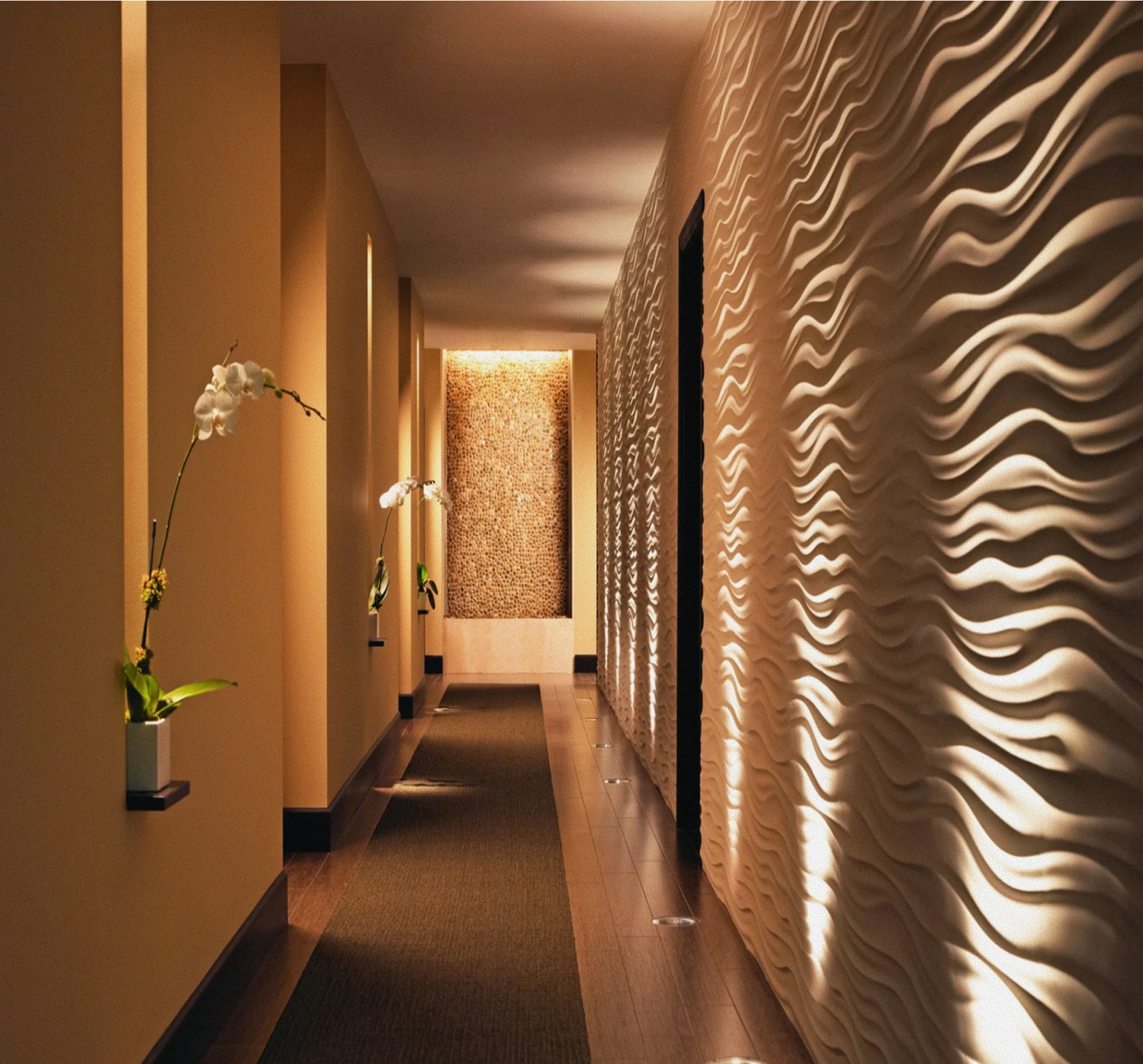 Dimly lit spa corridor with sculptural rippling wall panels, floor lighting, and white orchids at The Seagate Hotel