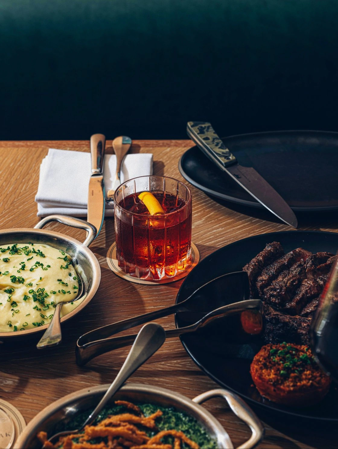 Overhead table spread of steaks, sides, and cocktails at Bourbon Steak by Chef Michael Mina at The Seagate Delray