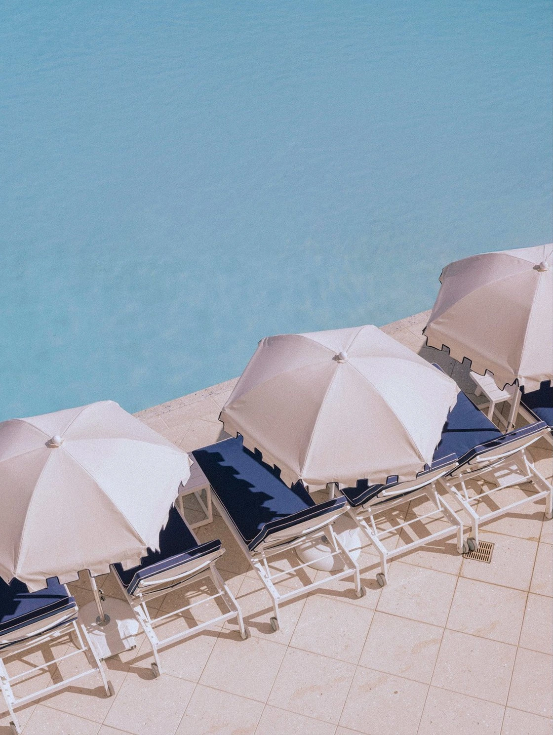 Overhead view of white umbrellas and navy lounge chairs lining the pool deck at The Seagate Beach Club