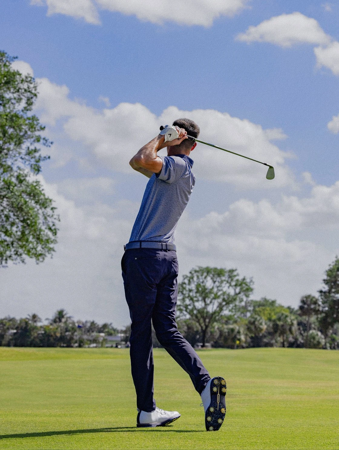 Man mid-swing on the fairway at The Seagate Golf Club under a blue Florida sky
