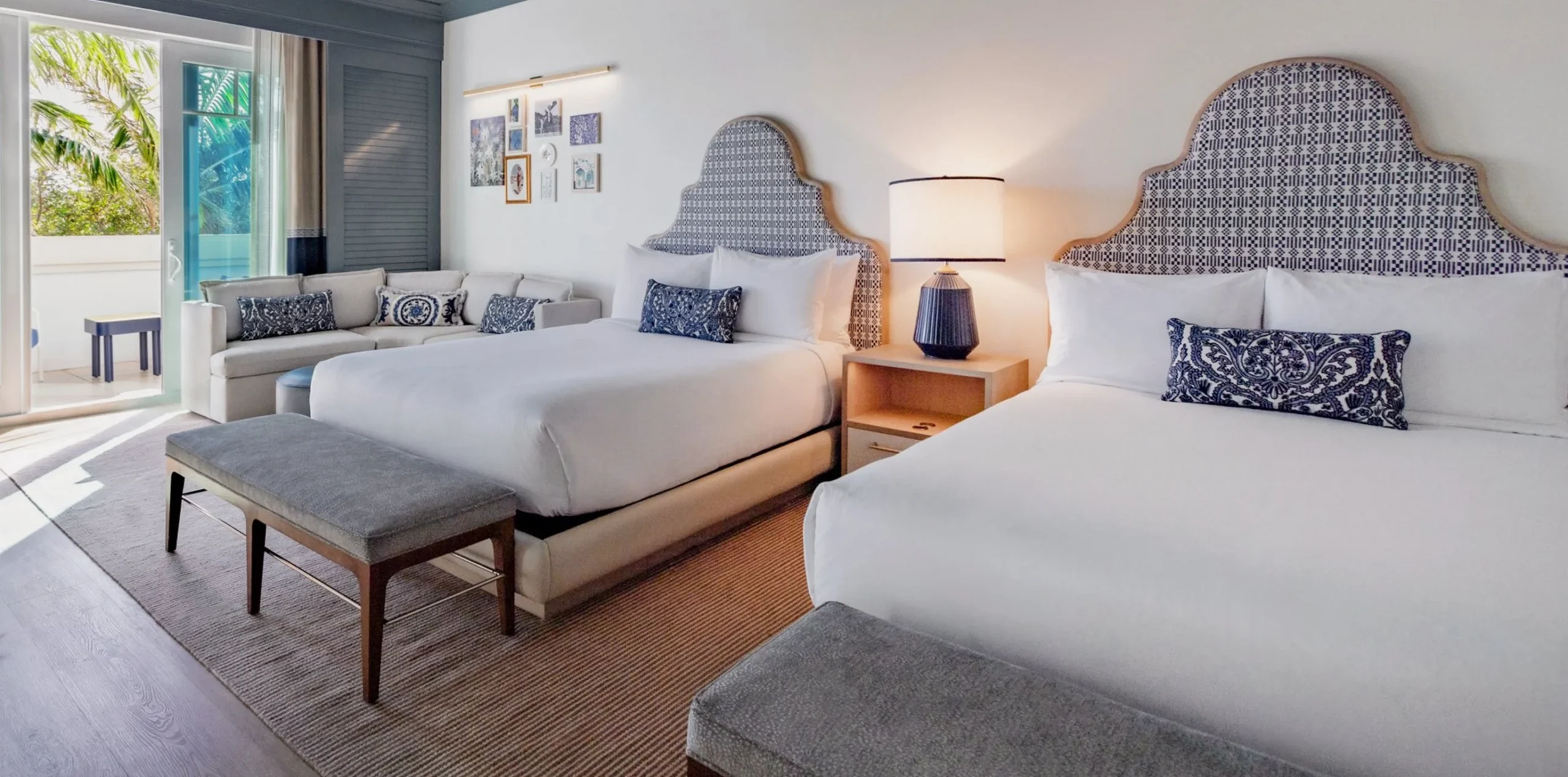 Two queen beds with blue and white patterned headboards in a bright Seagate Hotel deluxe room with a private balcony