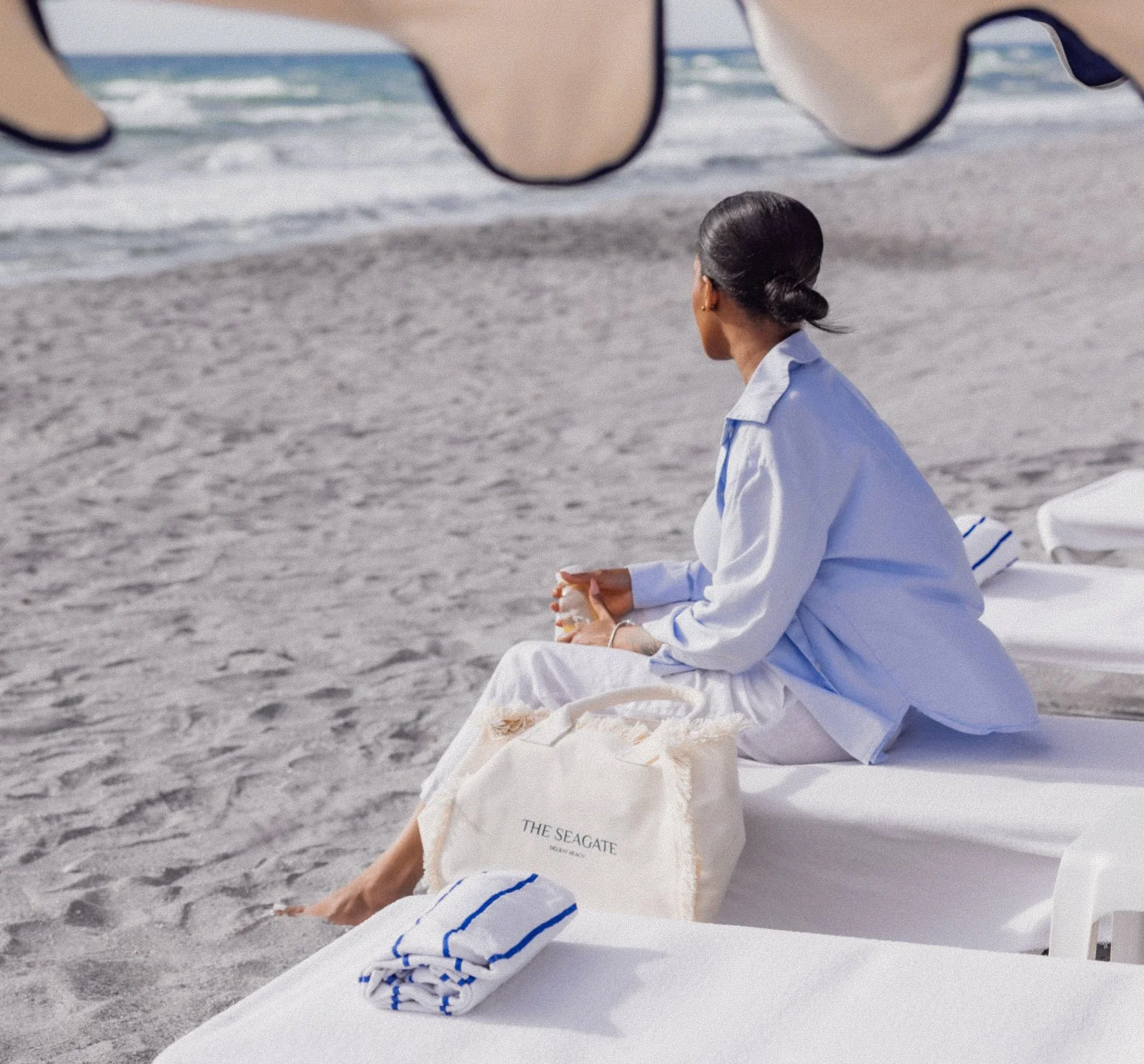 Woman seated on a white beach lounger in a blue shirt with a branded Seagate tote bag on the private member beach