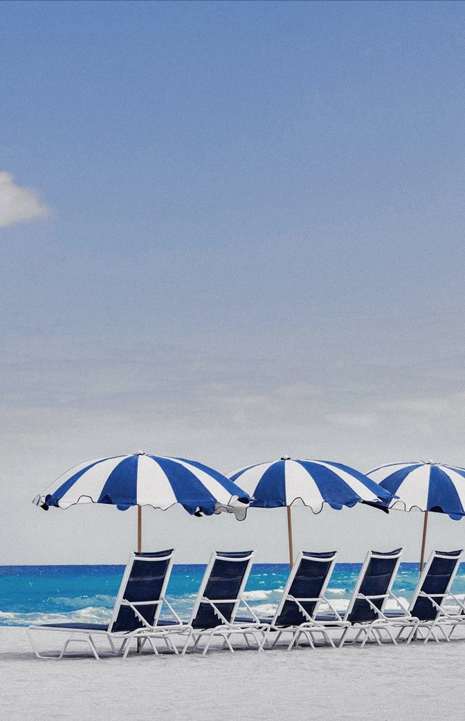 Six navy beach loungers under three blue and white striped umbrellas on the private member beach at The Seagate, ocean in background